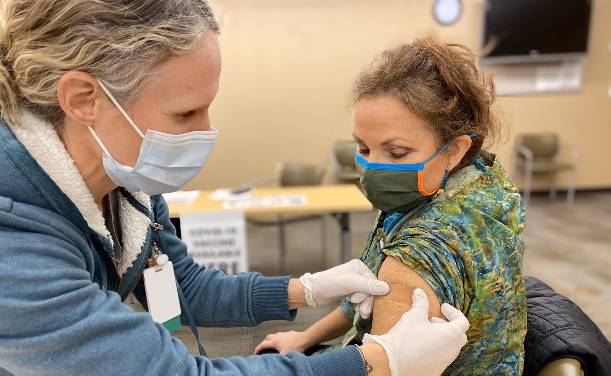 Healthcare professional places band aid on arm of recently vaccinated woman.