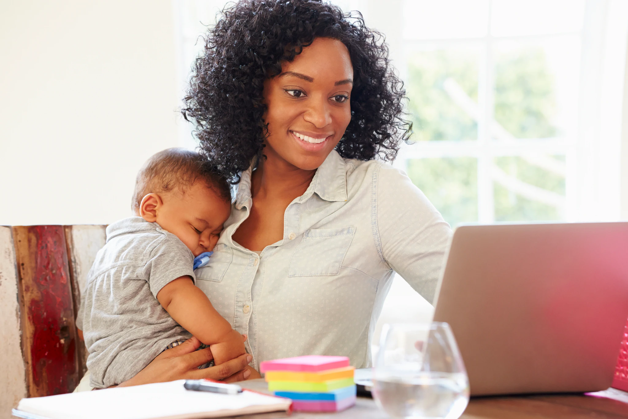 Mother and sleeping baby Woman holding sleeping baby while she uses her laptop.