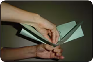 A person folds sheets of green paper to form a paper cabbage