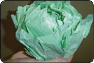 A person folds sheets of green paper to form a paper cabbage