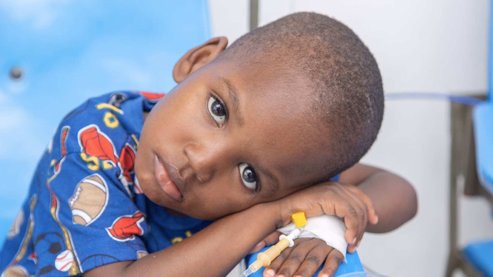 Young boy with his head resting on his crossed arms and being treated for cholera through an IV