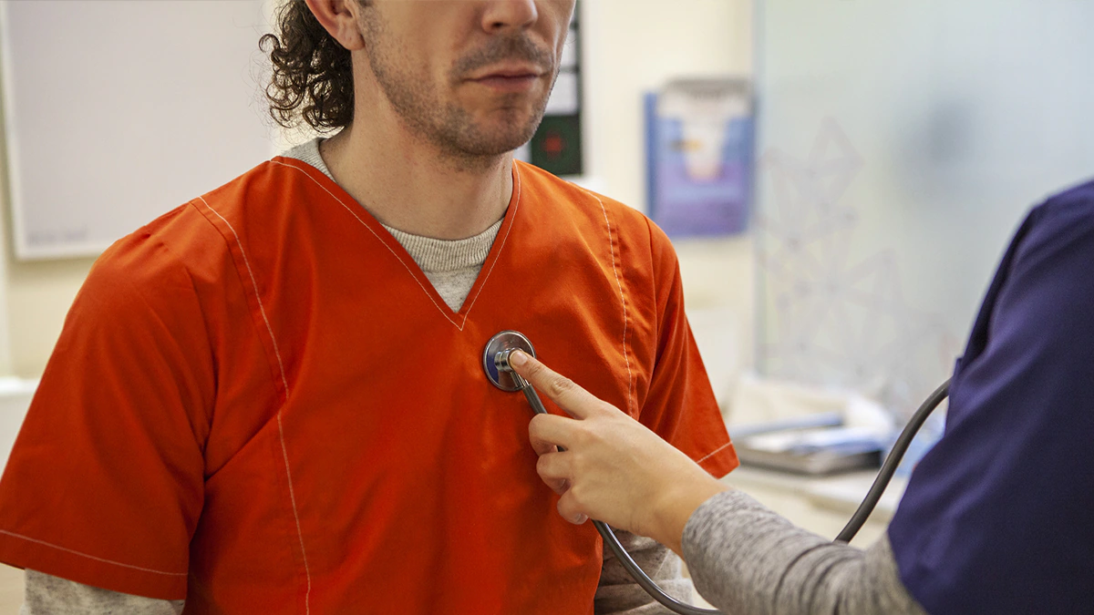 — title missing — A close-up photo of a physician checking the pulse of a person wearing an orange shirt.