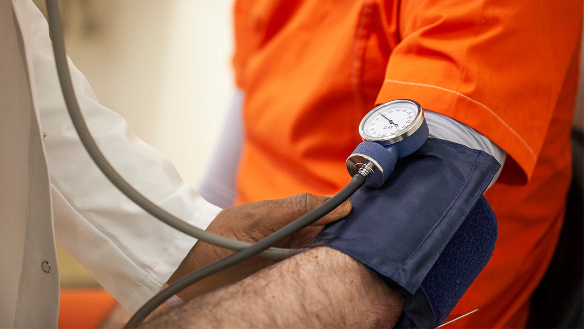 — title missing — An incarcerated person in an orange jumpsuit receives a blood pressure test from a doctor.