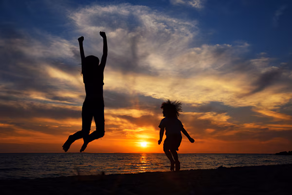 Happy young family have fun on beach and jump at sunset
