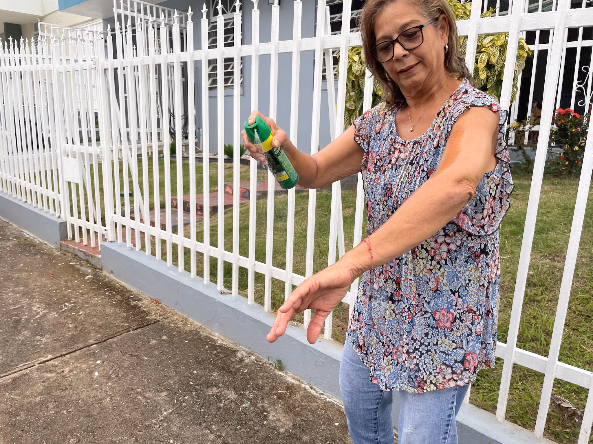An older woman sprays insect repellent on her arm.