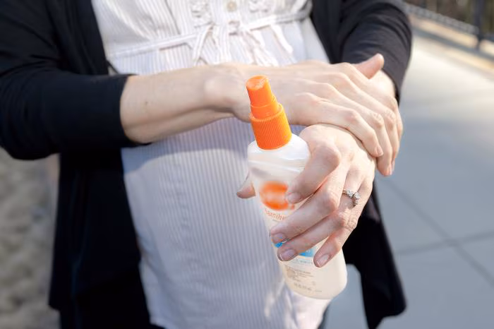 A pregnant person applying insect repellent.