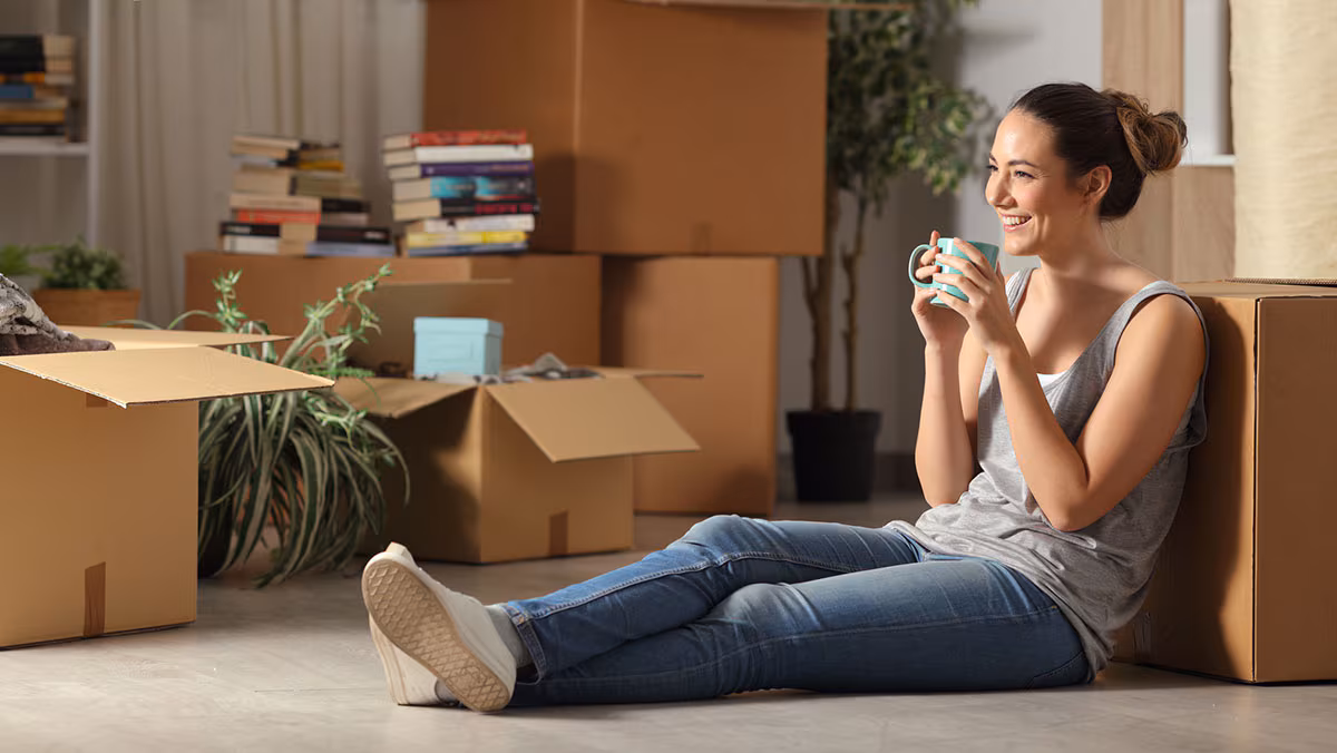 Young adult girl sitting on the ground drinking coffee with boxes around her