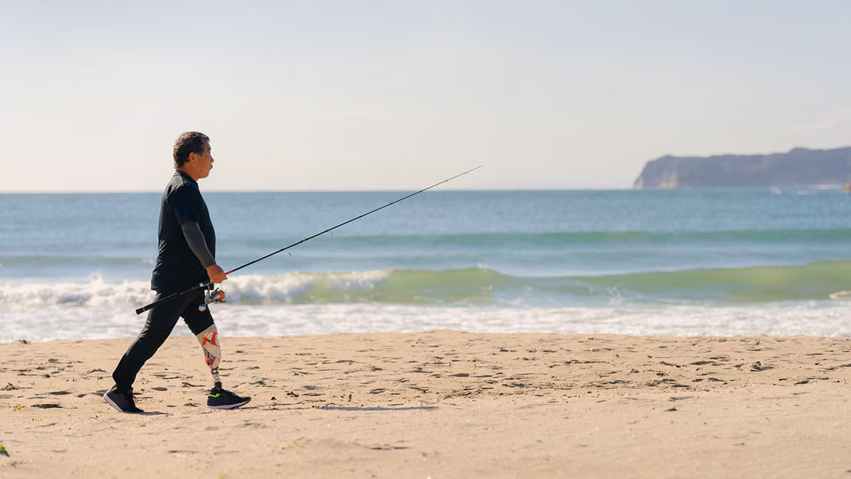 Senior man with artificial leg walking at beach with fishing rod man walking on the beach with a prosthetic leg