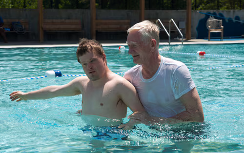A man helps a boy with Down Syndrome in a pool.
