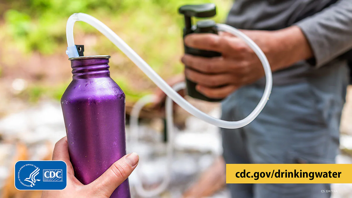 Filter water on trail 1200x675 Hikers pumping water from a stream into a filter. A tube from the filter moves filtered water into a reusable water bottle.