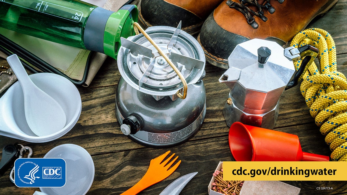 Camping supplies to treat water 1200x675 Table with camping supplies on it, including a portable gas stove, water kettle, water bottle, matches, hiking boots, bowls, and utensils.