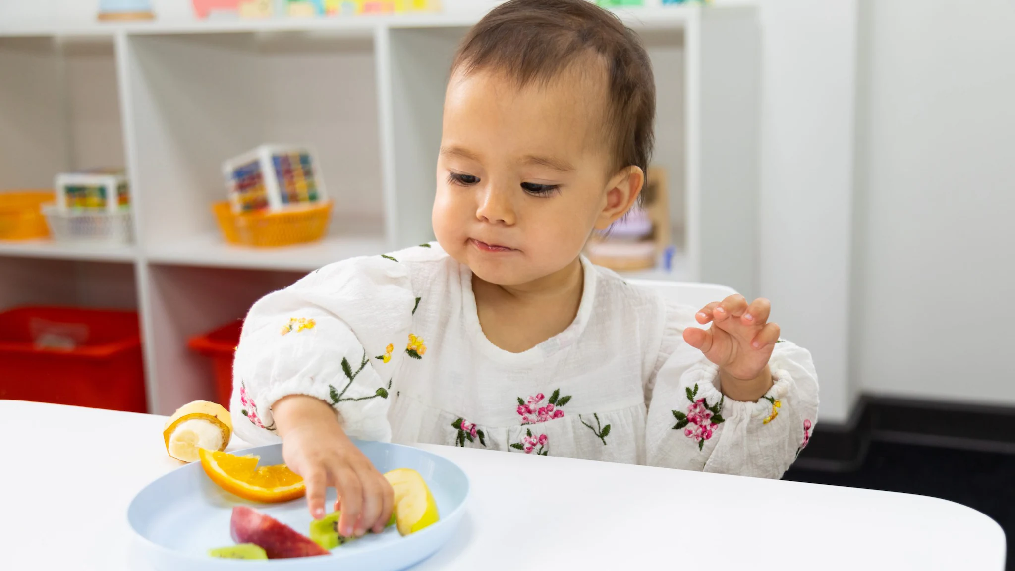 — title missing — Young child in early care and education setting eating from a plate of fruit.