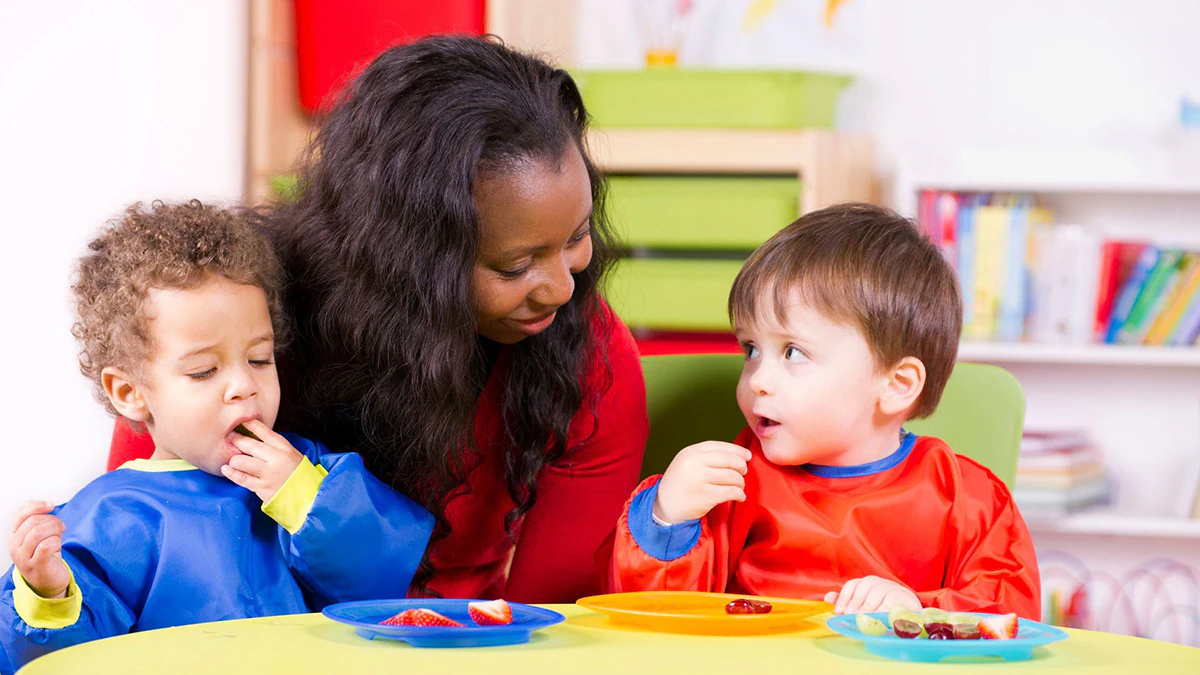 Daycare worker with children Children eating fruit at a nursery with their care giver