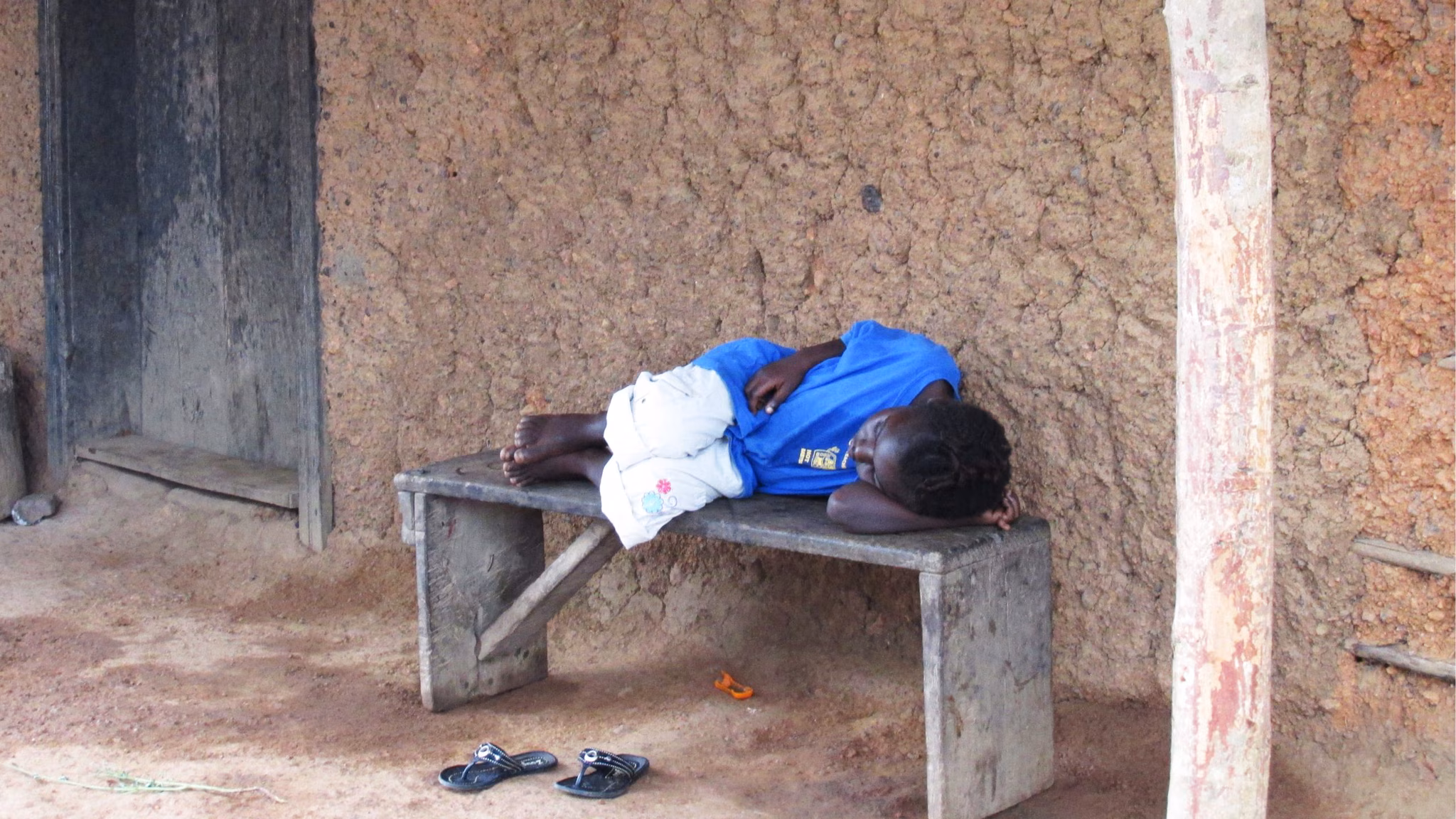 A sick young girl lies on a wooden bench