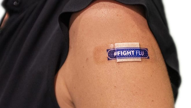 A person is wearing a black shirt and has a bandage on their upper arm that reads "FIGHT FLU." A person is wearing a black shirt and has a bandage on their upper arm that reads "FIGHT FLU."