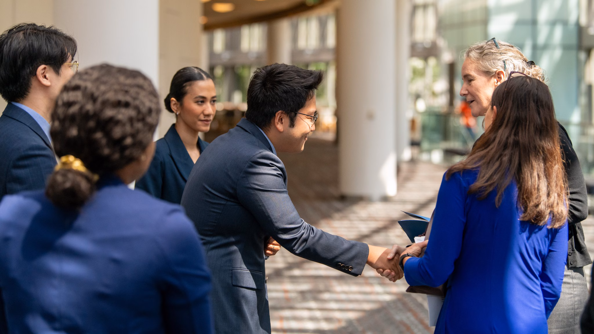 A group of men and women of all ethnicities standing in a group while two members shake hands