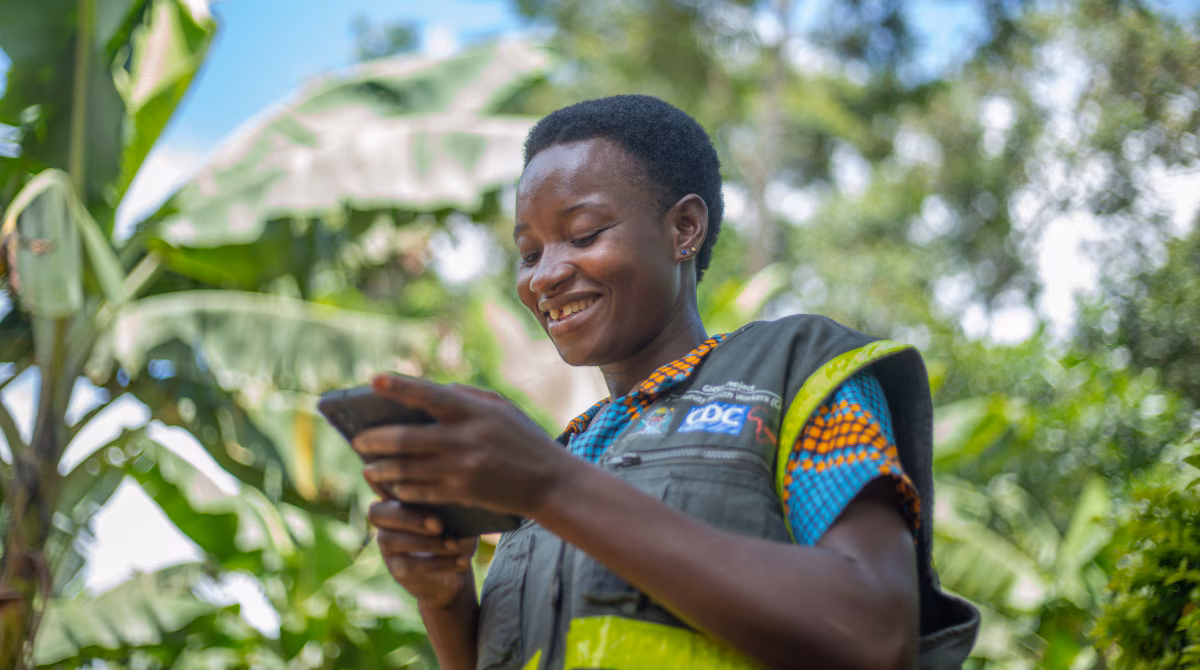 Woman wearing a CDC vest smiles as she holds electronic device.