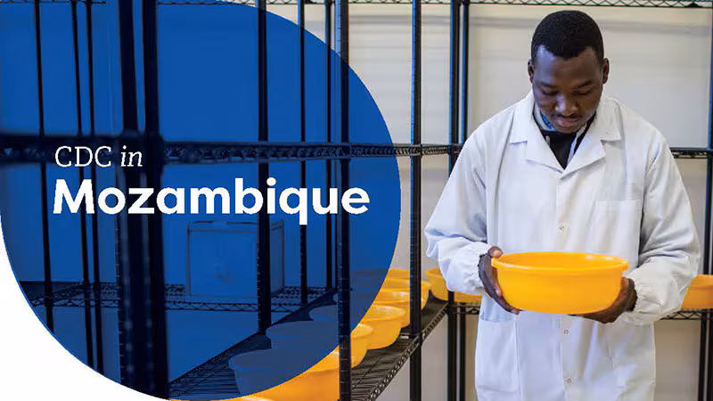 Lab technician in a white coat holding a yellow container, labeled "CDC in Mozambique."