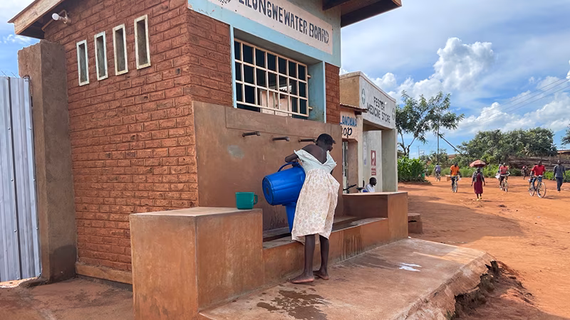 A person holds a bucket while standing in front of an outdoor water station