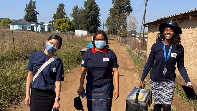 Eswatini_PopulationSurvey_Photo_2024 Three CDC professionals stand outdoors on a dirt road.