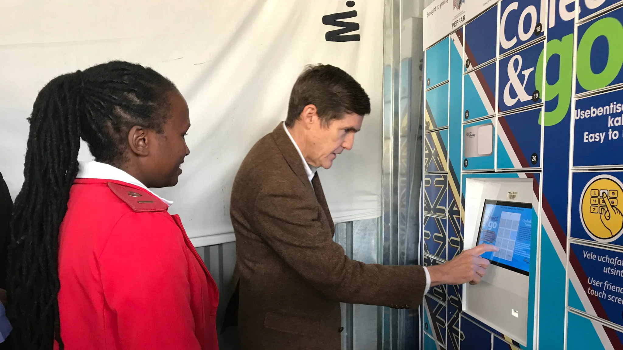 Eswatini_USAmbLulaMeds_Photo A man touches a screen display with his finger. A person stands behind him and looks on.