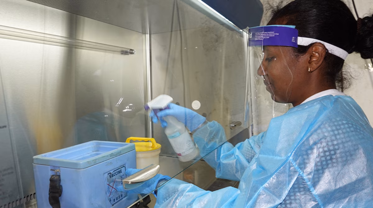 Woman lab worker dressed in personal protective equipment sprays a container in a laboratory setting.