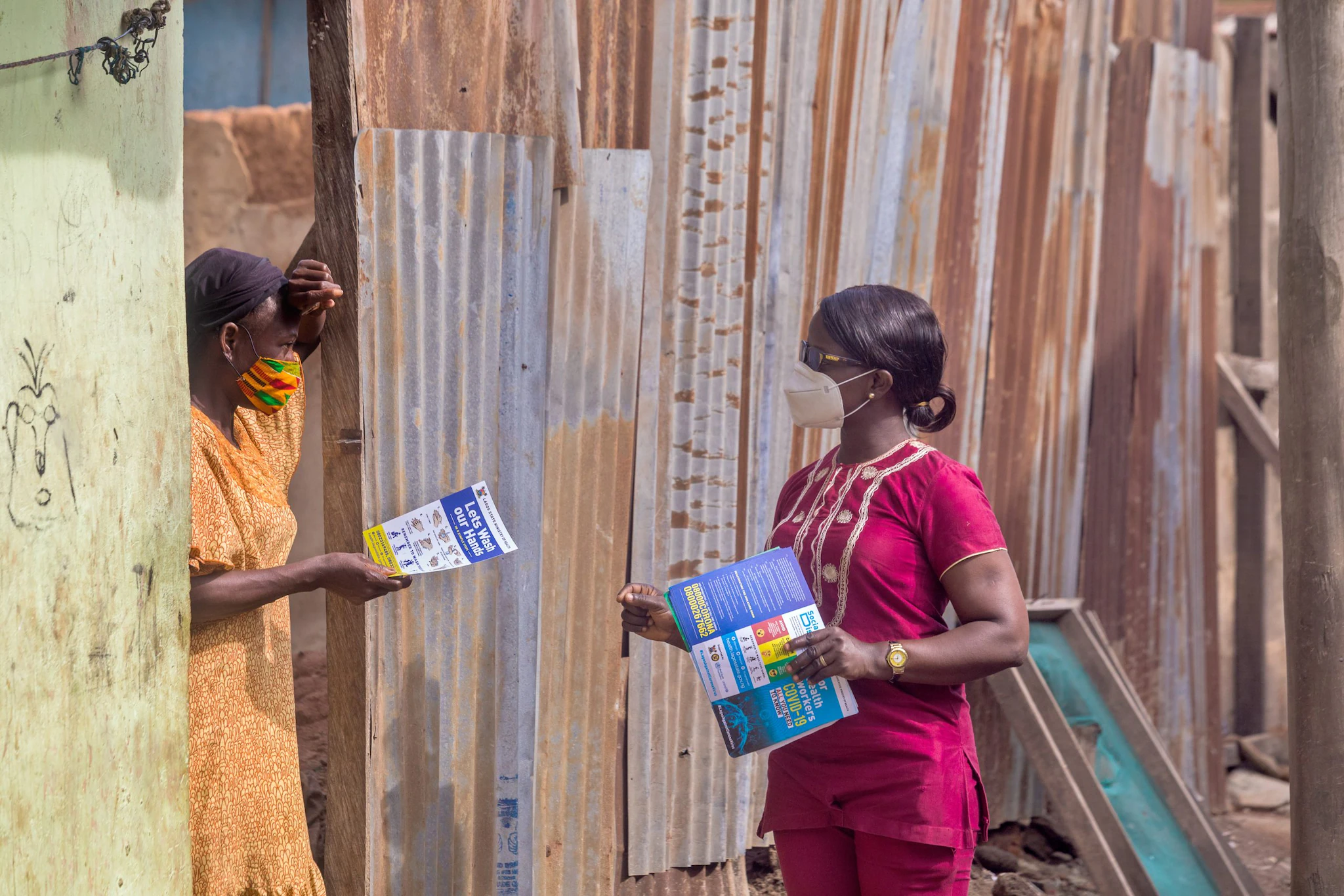 -- title missing -- Two people talk outdoors while holding printed documents about handwashing and COVID-19 prevention.