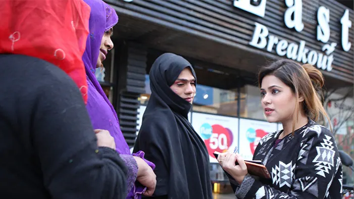 Pakistan_Epidemiology_FieldPhoto A woman in a city with a clipboard and pen, talking to women wearing a hijab