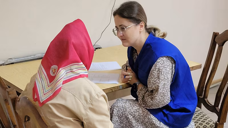 Two people are seated at a table and talking with one another.