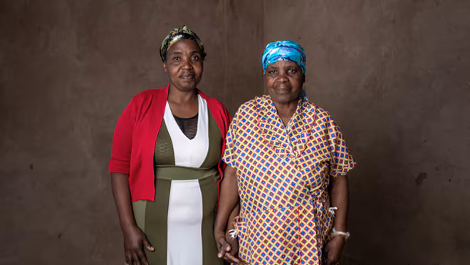 Two sisters stand side by side holding hands.