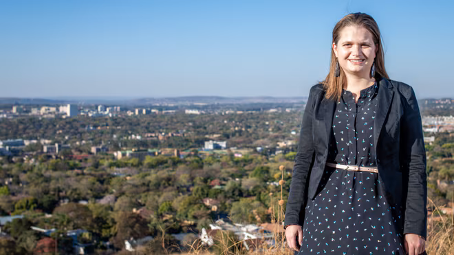 Cheryl is standing under an open clear sky next to bushes
