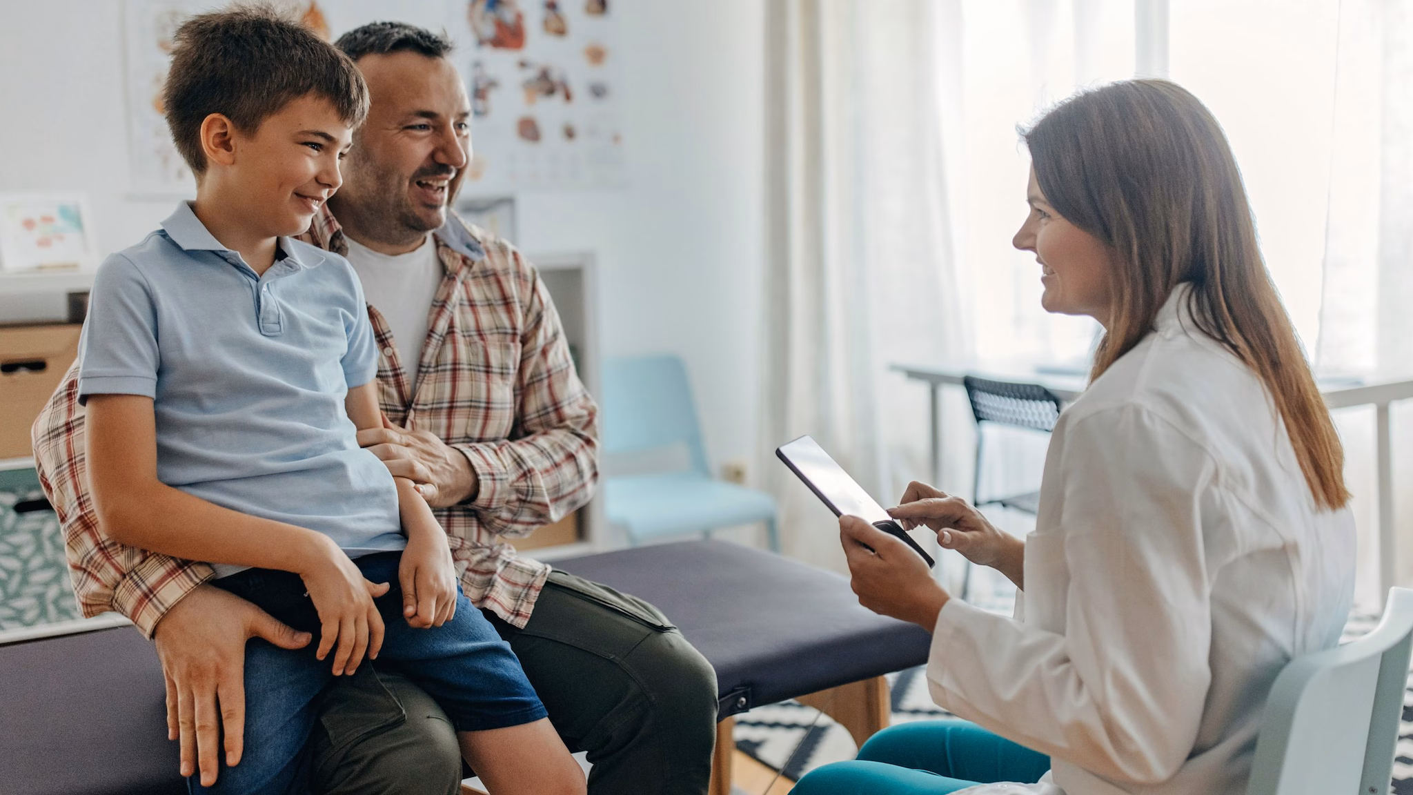 Health care provider goes over chart with father and son in a medical setting.