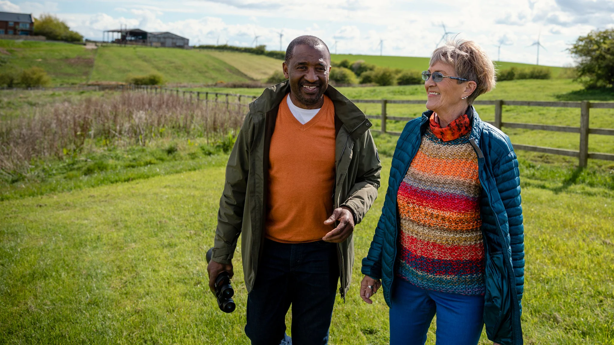 -- title missing -- Two people walking and talking in a field in a rural setting.