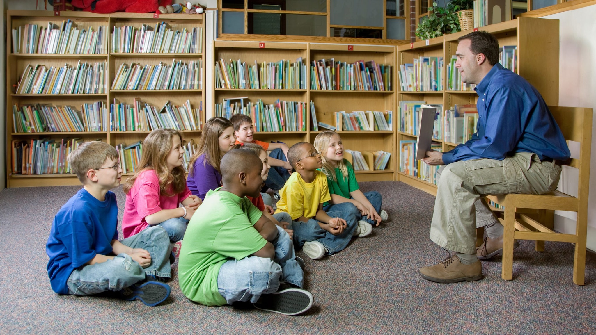 Parent-Reading_story-time-16x9 Teacher talking with a group of students in school library.