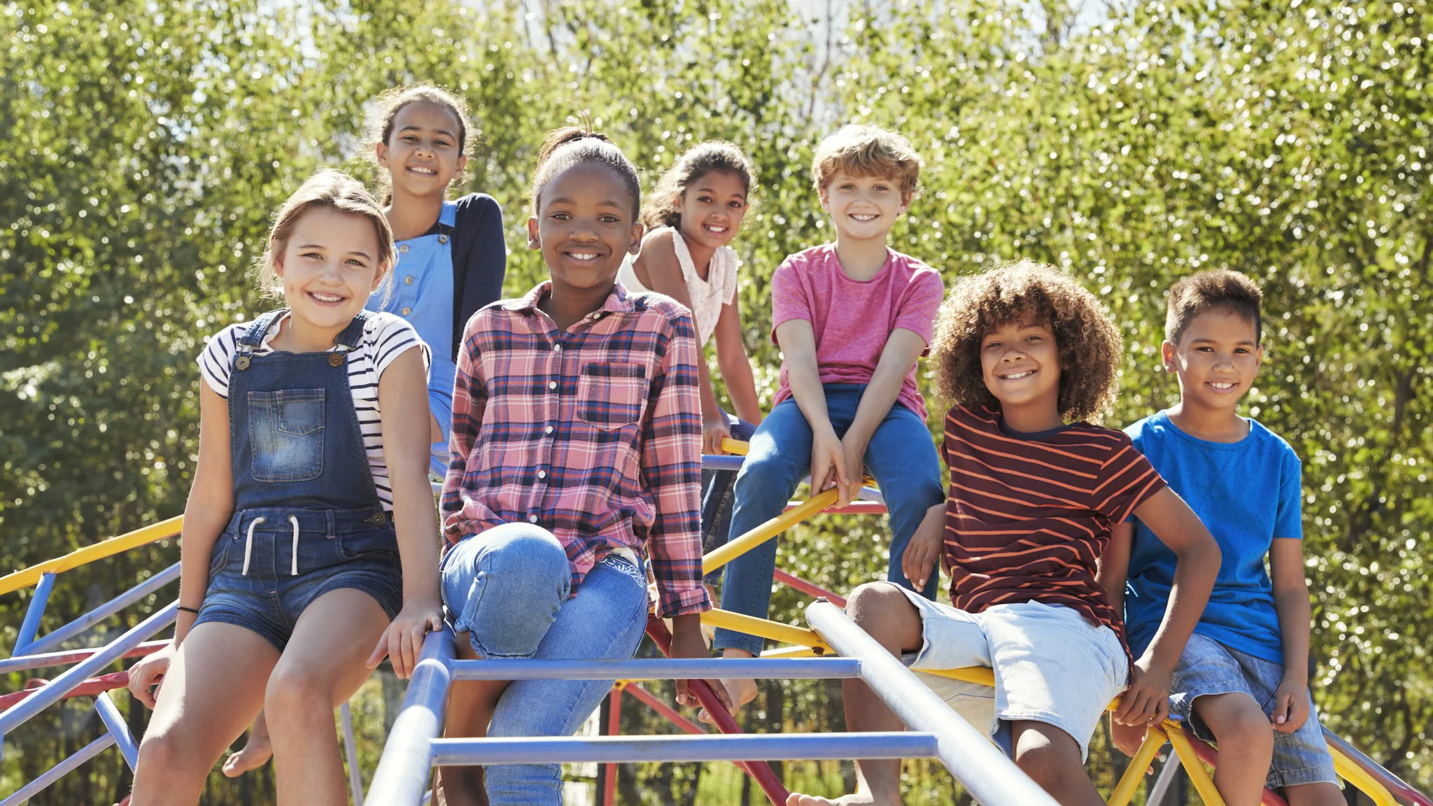 Pre-teen friends sitting on climbing frame in playground A group of pre-teens siting on a playground climbing frame, smiling.