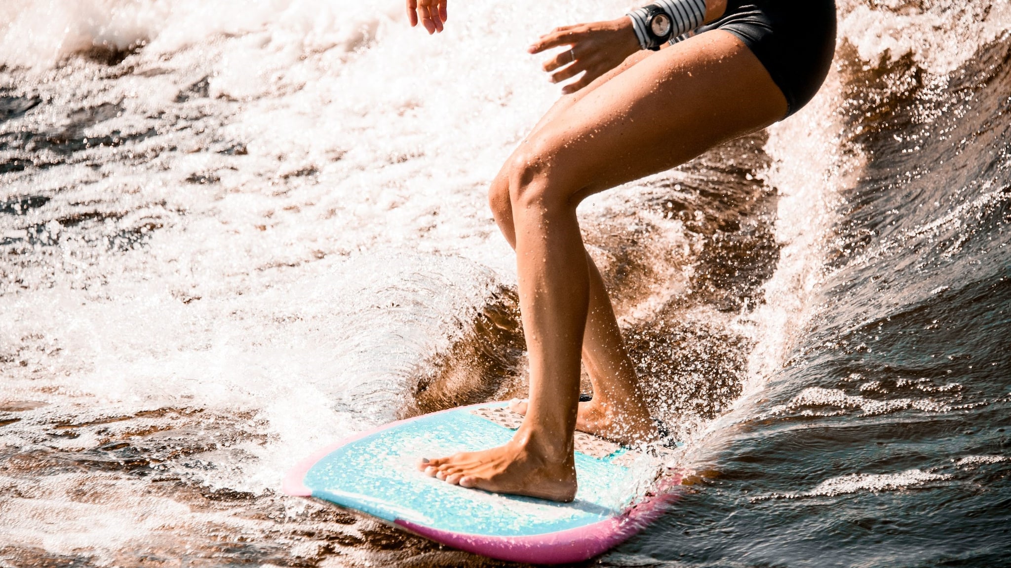 Surfing image A close up picture of the legs of a person surfing with water spray behind their surfboard.