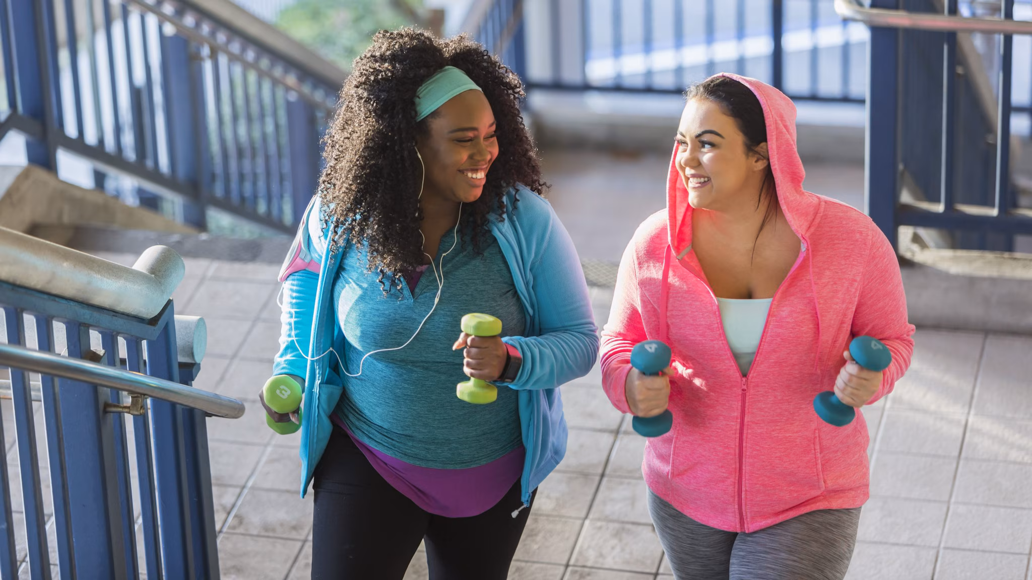 — title missing — Two women walking up stairs while carrying hand weights.