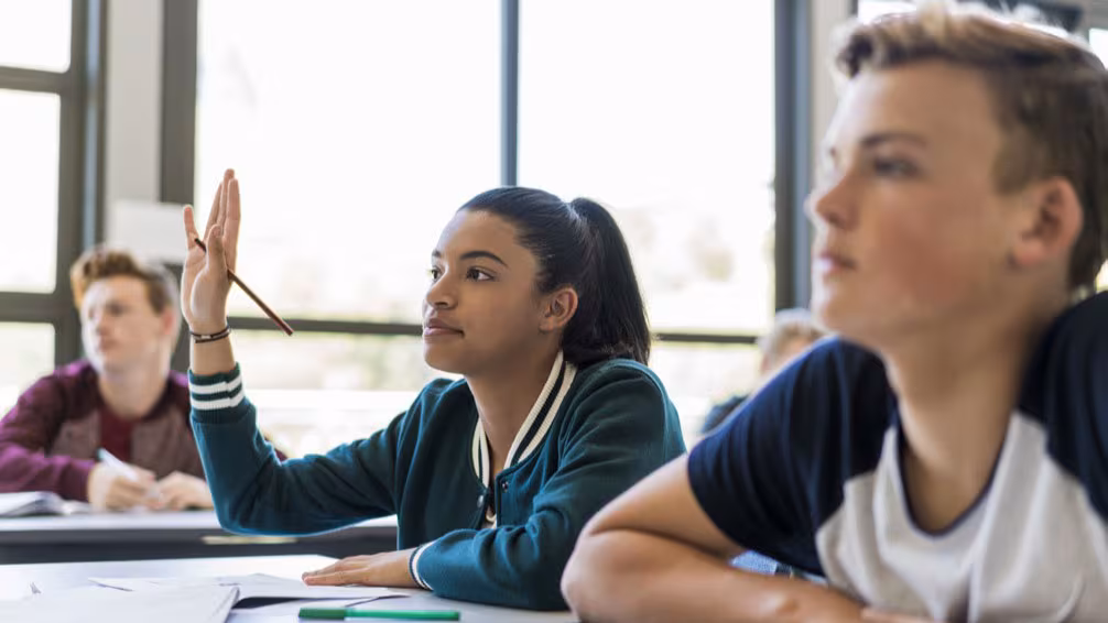 Teen mental health A female high school student raises her hands in classroom.