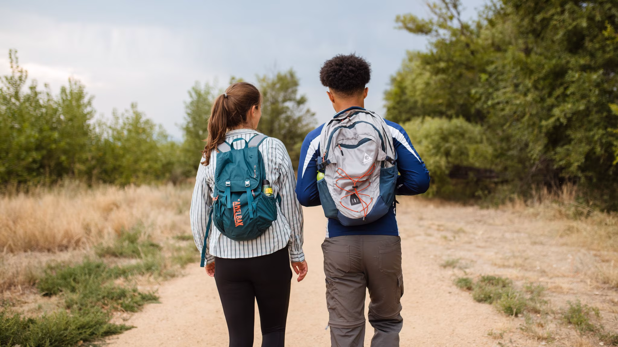 Two people walking on a trial with backpacks on.