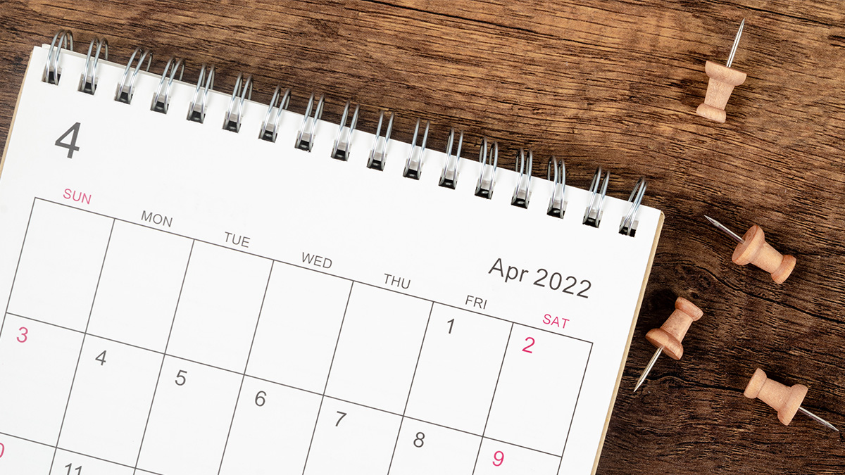 A calendar sitting on top of a desk showing April 2022 with four thumb tacks to the right of it