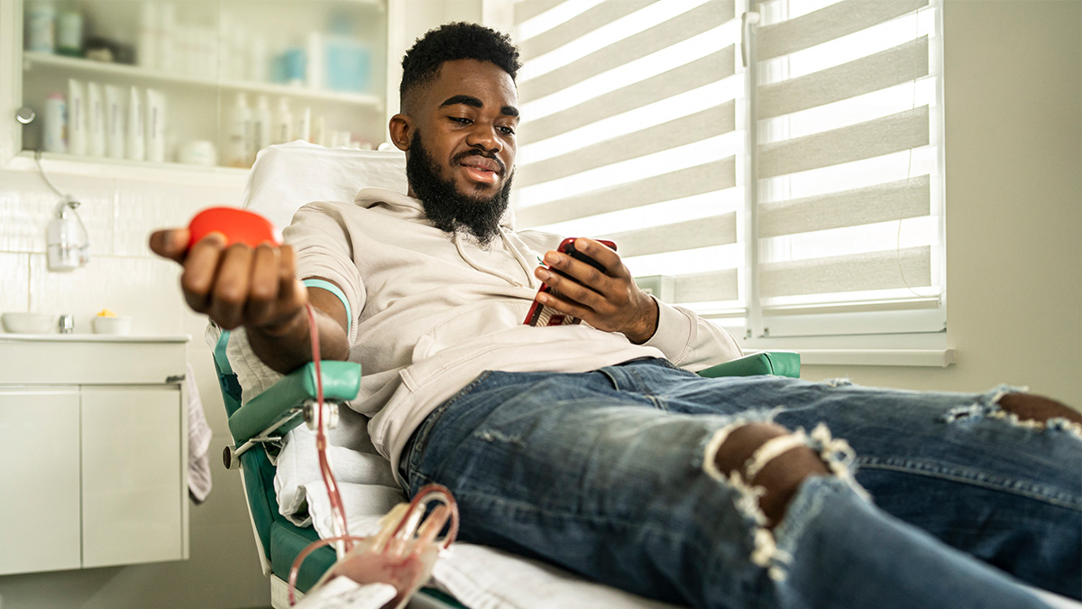Reporting HBV and HCV Infections in Repeat Blood Donors Thumbnail A man looking at his phone while giving blood in a doctor's office