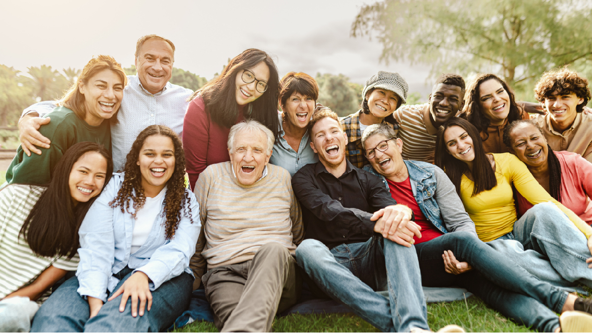 Age Group of people sitting together on the grass, smiling.