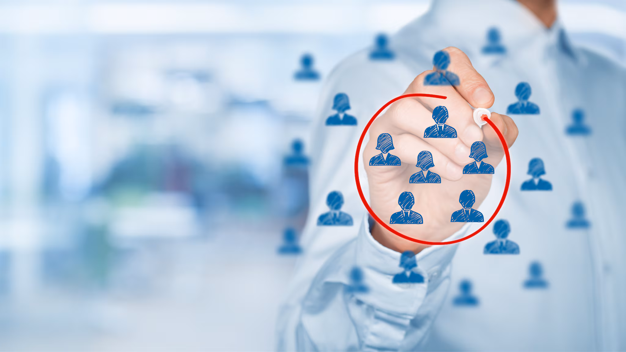 A hand, holding a pen, draws a red circle around a group of blue heads, which are surrounded by more blue heads, on a translucent screen.