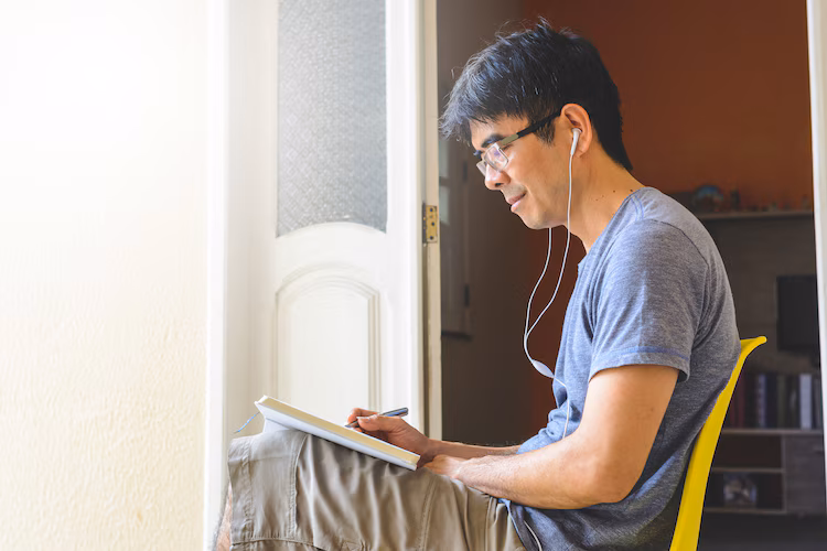Asian man sitting with a book and headphones
