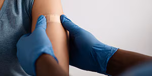 patient-vaccination Hands of a doctor in protective gloves puts band aid to inculcate site to patient in clinic.