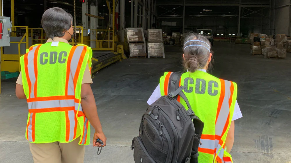 cdc importation Workers wearing CDC vests walk toward a warehouse.