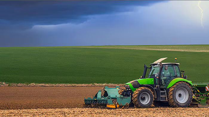 Tractor outside Tractor working through an empty field while there are stormy clouds and lightning in the sky.