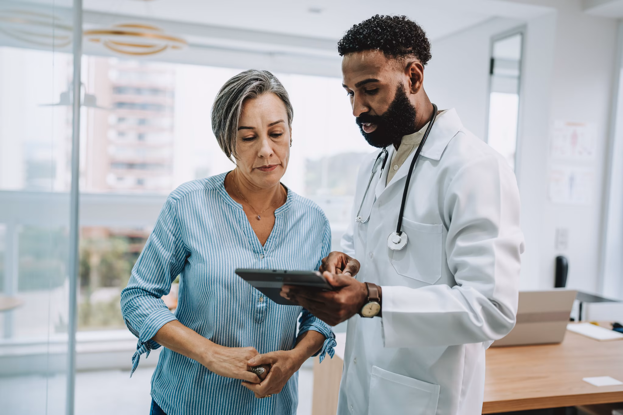 Clinical Overview A doctor speaking to a patient. They are both looking at a tablet while standing up.