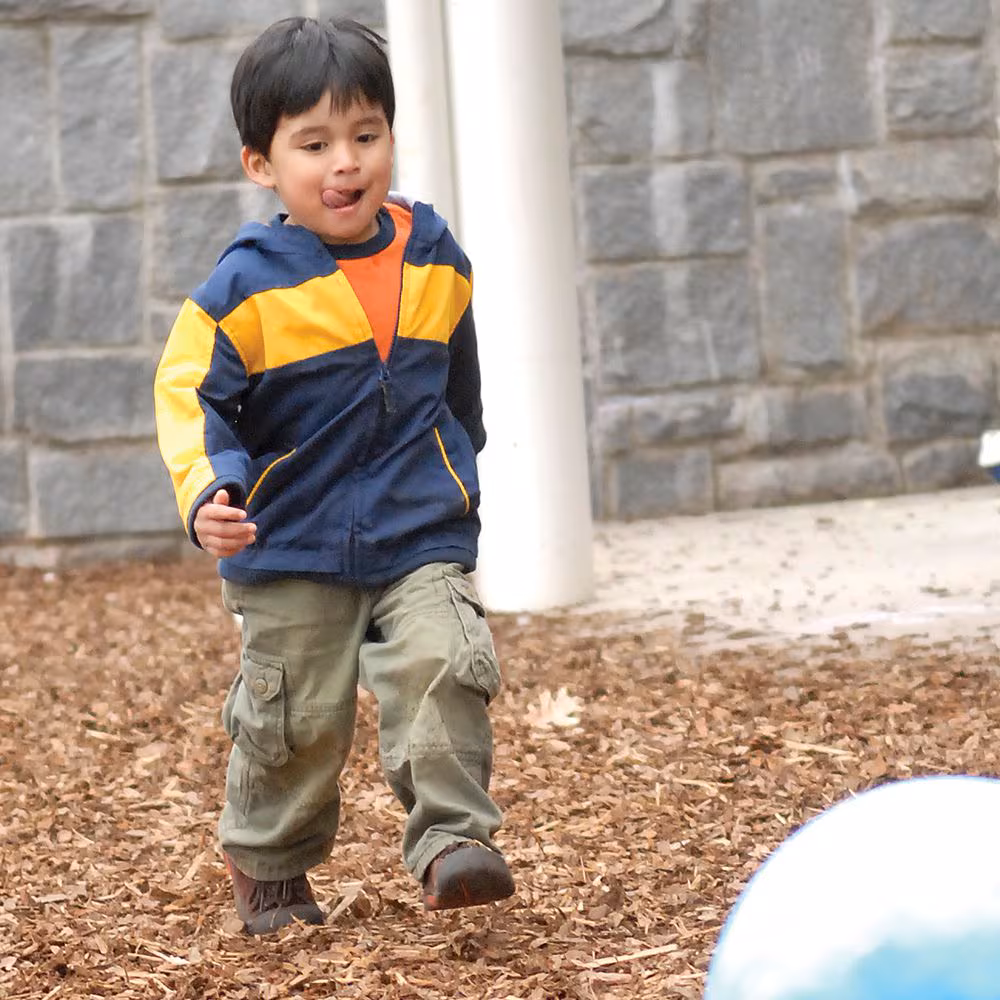 A boy runs across the play ground at daycare.