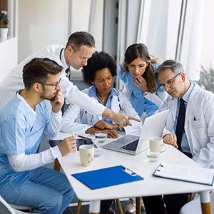 Physicians and nurses meeting and discussing item on laptop.